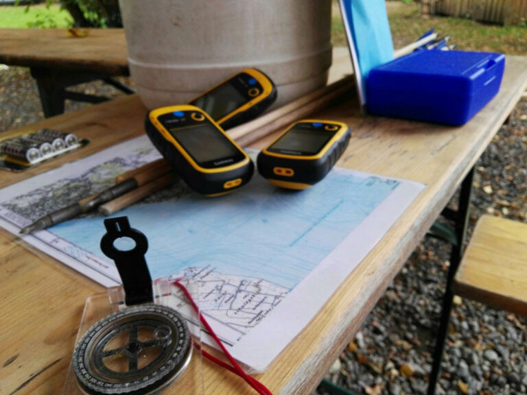 Wanderausrüstung mit GPS, Karte und Kompass auf Tisch.