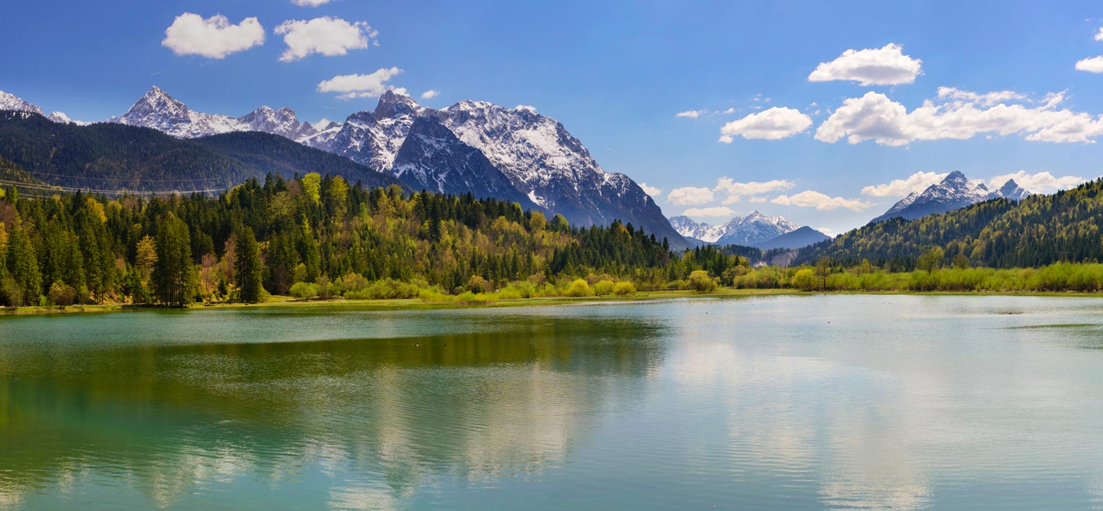 Bergsee mit Wald und schneebedeckten Gipfeln