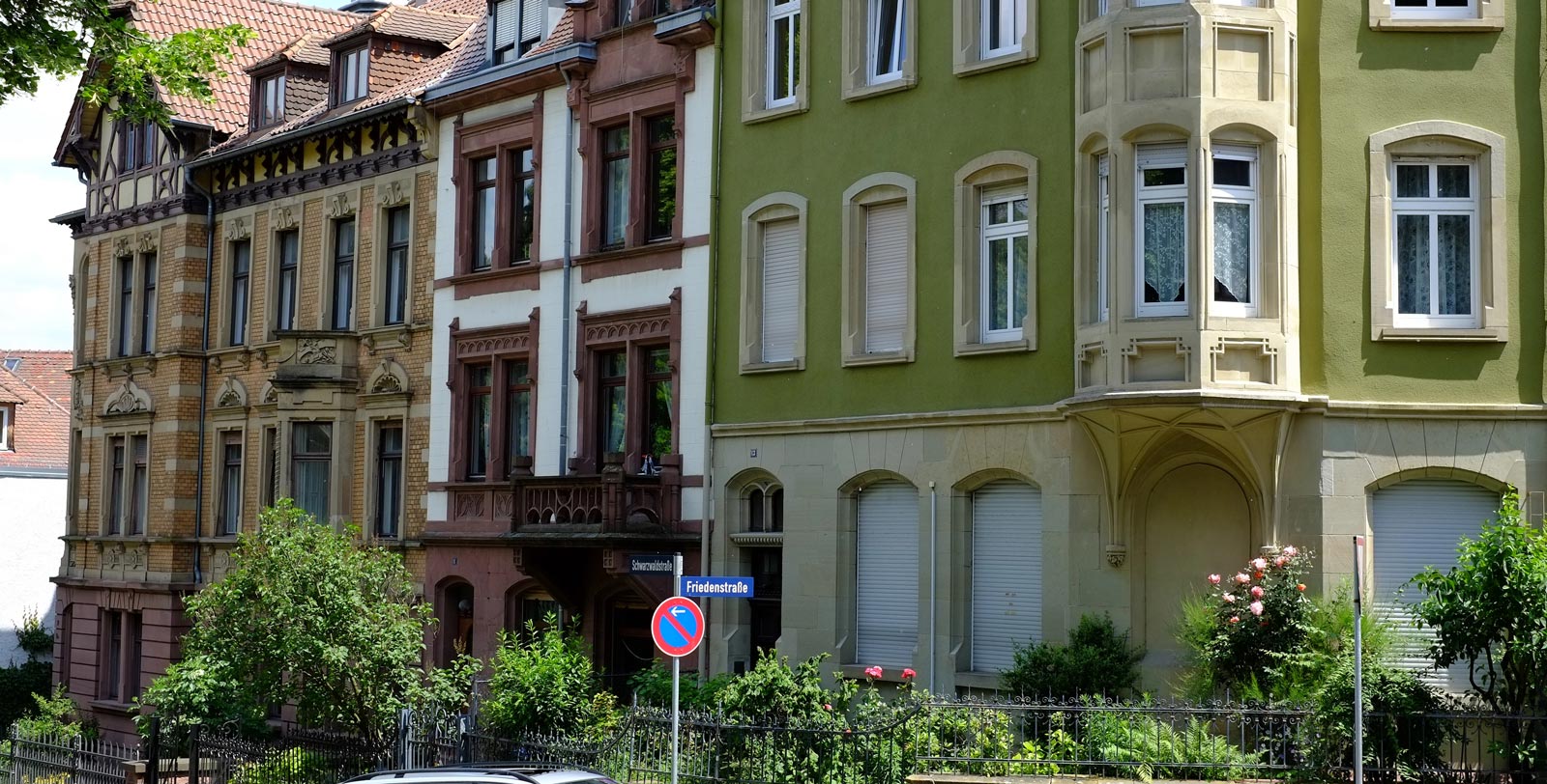 Mehrstöckige Altbauten mit grüner Fassade und Bäumen.